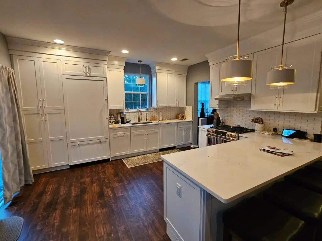 A kitchen with white cabinets and wood floors.