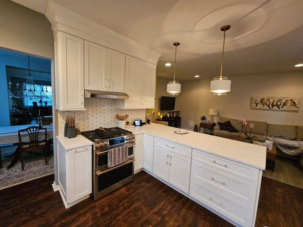 A kitchen with white cabinets and wood floors.