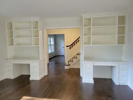 A room with white built in bookcases and wooden floors.