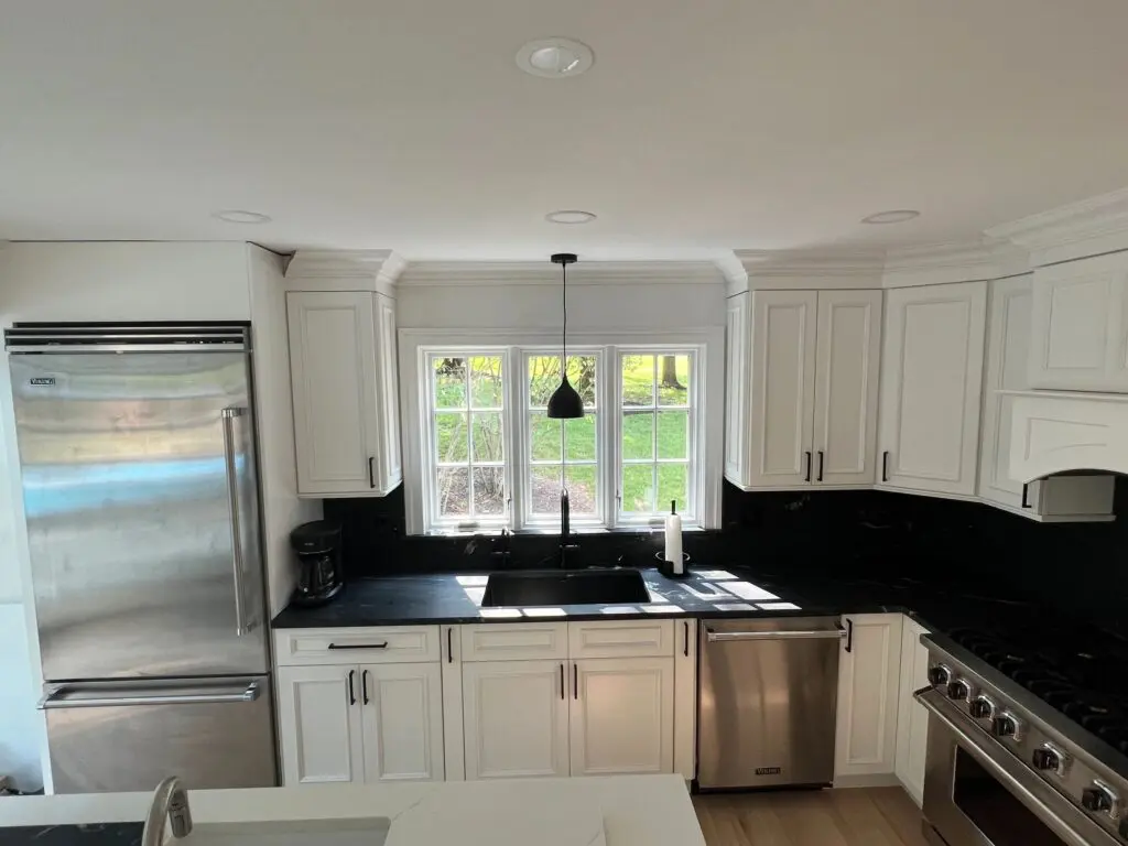 A kitchen with white cabinets and black counter tops.