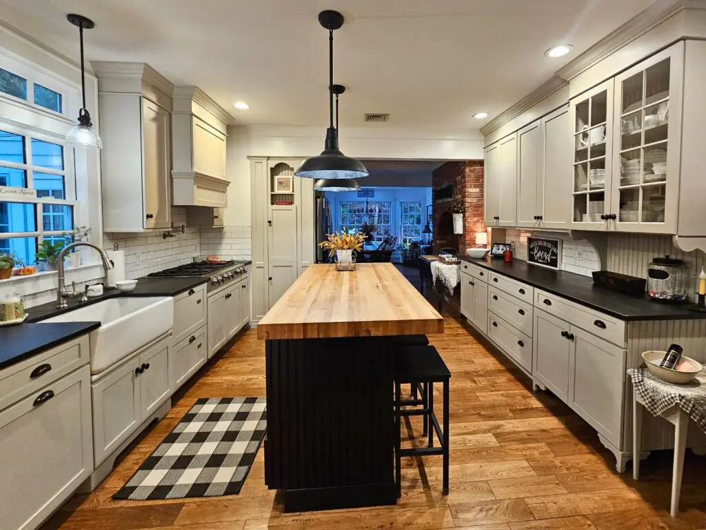 Impecca-Bull kitchen with sage green shaker cabinets. Black island in center of galley kitchen.