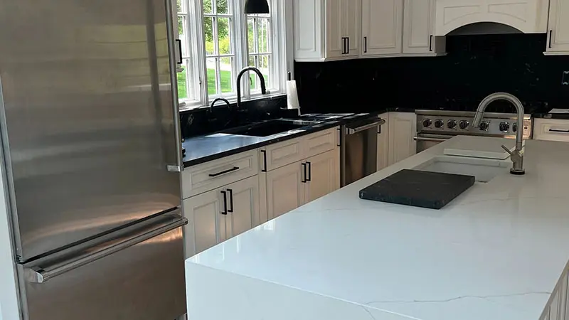 A kitchen with white cabinets and black counter tops.